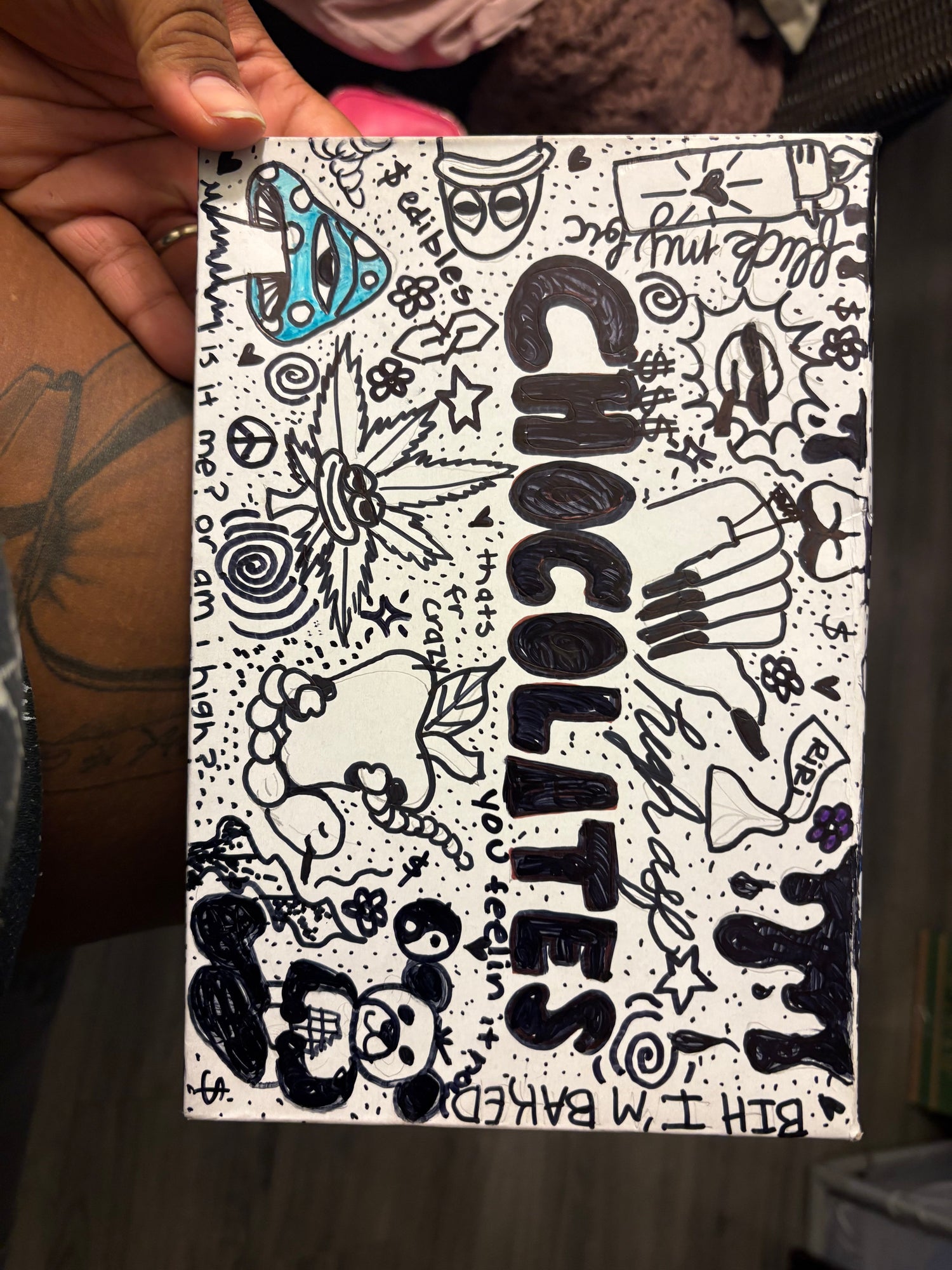 Handmade sign with black and white doodles and text, held by a person.